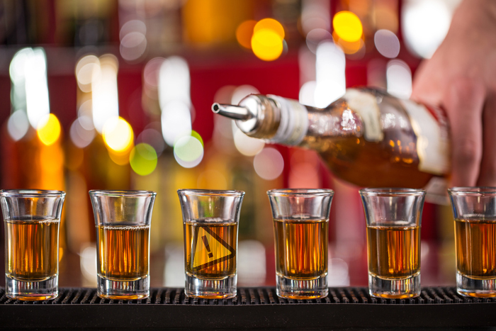 photo of bartender pouring alcohol into a row of shot glasses