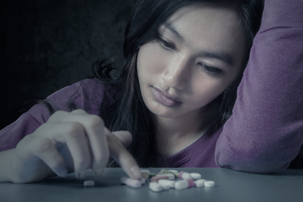 photo of a young woman with a pain pill addiction looking at a pile of different painkillers represents need for pain pills detox